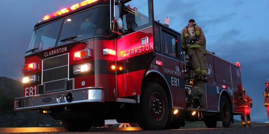 Firefighters stand around Clarkston Fire Department engine E81 in the evening with the emergency lights on