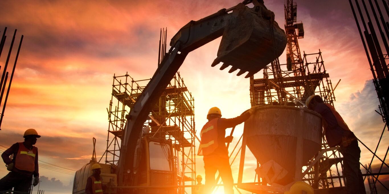 Group of construction workers manage a worksite at sunset, with an excavator and a cement mixer