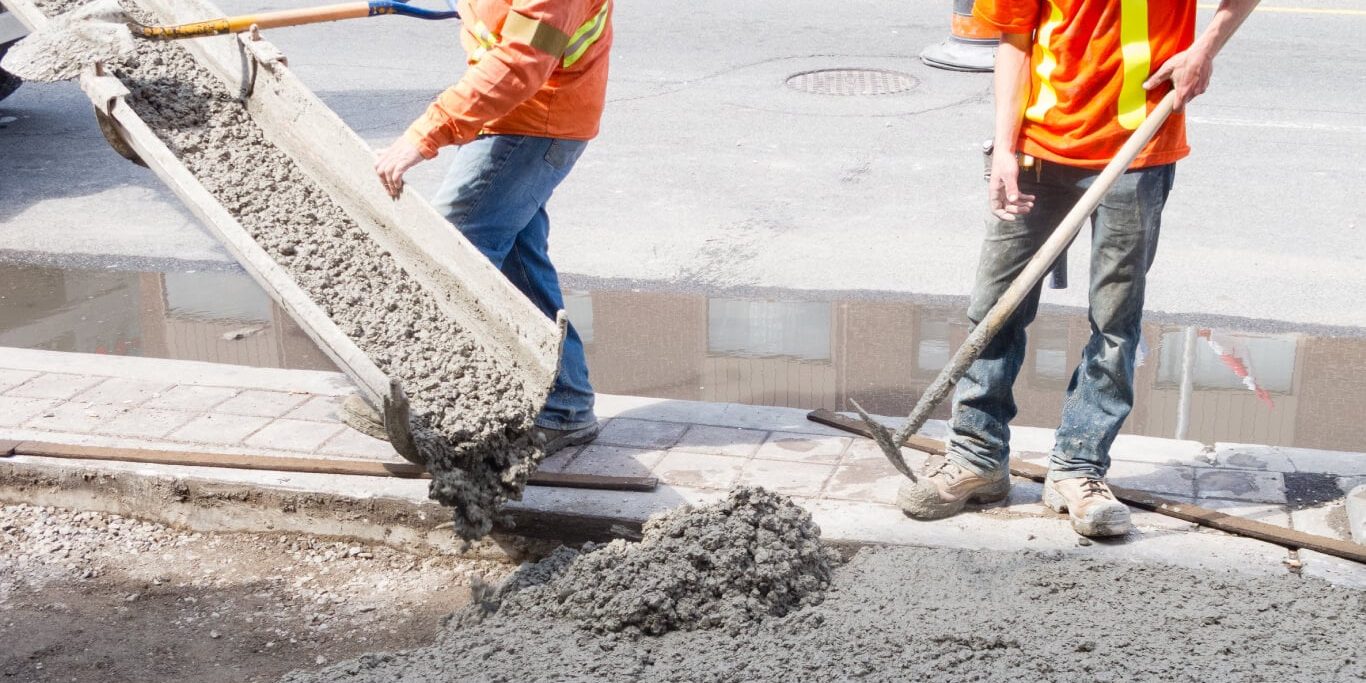 Two public works employees pouring concrete for a sidewalk